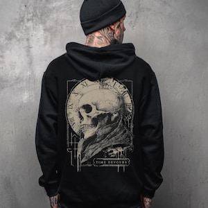 May include: Black hoodie featuring a detailed graphic of a skull within a clock face, with Roman numerals and the text "TIME DEVOURS." The design is in shades of gray and beige. The hoodie has a hood and a drawstring.