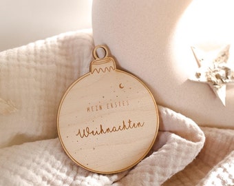 Può includere: Un ornamento di legno a forma di palla di Natale con il testo "Mein erstes Weihnachten" (Il mio primo Natale) in tedesco.