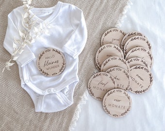 Può includere: Dischi in legno per i traguardi del bambino con un design floreale e le parole "Hallo kleines Wunder", "ein Monat", "zwei Monate", "drei Monate", "vier Monate", "fünf Monate", "sechs Monate", "sieben Monate", "acht Monate" e "neun Monate".
