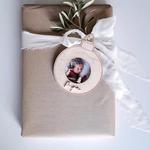 Pu&ograve; includere: Un ornamento natalizio in legno a forma di sfera con una cornice per foto. L'ornamento &egrave; decorato con il testo "Frohe Weihnachten" e "Papa". Un bambino &egrave; ritratto nella cornice.