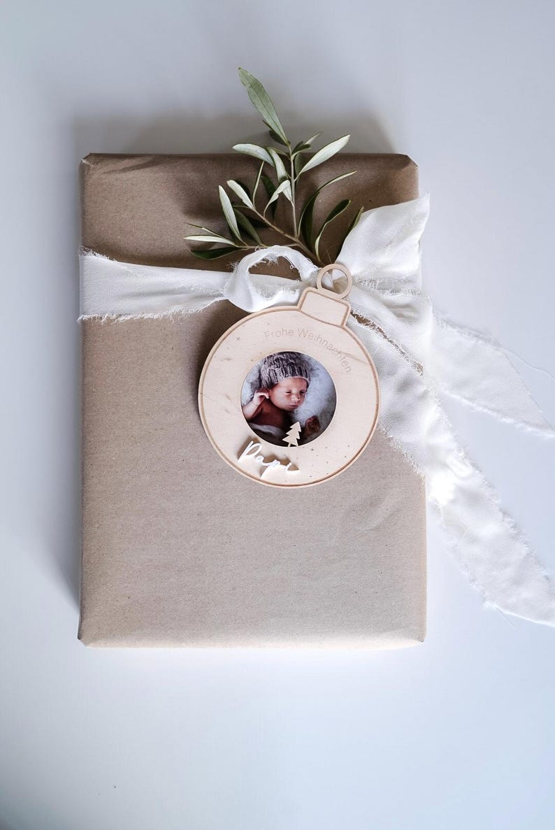 Pu&ograve; includere: Un ornamento natalizio in legno a forma di sfera con una cornice per foto. L'ornamento &egrave; decorato con il testo "Frohe Weihnachten" e "Papa". Un bambino &egrave; ritratto nella cornice.