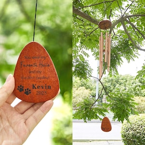 May include: A wooden wind chime with a teardrop-shaped pendant. The pendant is engraved with the text "You were my Favorite Hello and my Hardest Goodbye" and "Kevin 2025" along with paw prints. The wind chime has bronze-coloured tubes and is hanging from a tree.