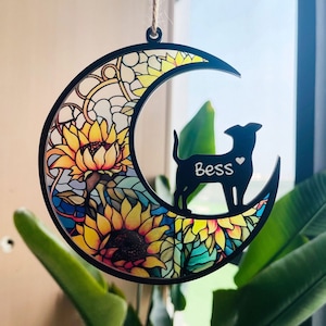 May include: A black wooden crescent moon ornament with a stained glass design featuring sunflowers and a silhouette of a dog with the name "Bess" written on it.