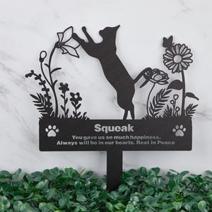 May include: Black metal garden memorial featuring a silhouette of a cat reaching for a flower. The memorial is inscribed with the text "Squeak" and the words "You gave us so much happiness. Always will be in our hearts. Rest in Peace."