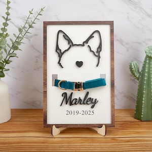 Può includere: Una targa in legno con una silhouette nera di una testa di cane, un collare blu turchese e il testo "Marley 2019-2025".