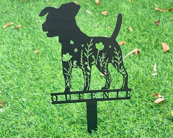 May include: Black metal silhouette of a dog with flowers and foliage inside the silhouette. The dog is standing on a metal base with the word "QUEENIE" written on it.