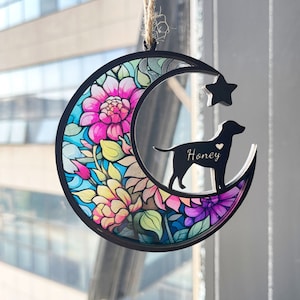May include: A black wooden crescent moon ornament featuring a colourful floral design and a black silhouette of a dog with the name "Honey" engraved on it.
