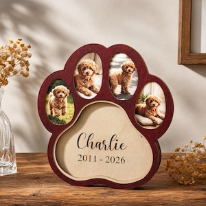 May include: A dark red wooden paw-shaped picture frame featuring three oval photo slots containing images of a small brown puppy. The central pad area is light beige and displays the name Charlie and the years 2011 - 2026 in black text.