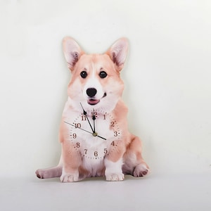 Może przedstawiać: Zegar ścienny z wzorem brązowego i białego psa rasy corgi. Tarcza zegara ma czarne wskazówki i czarne cyfry.