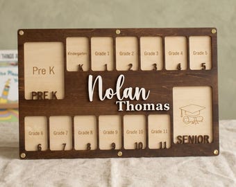 May include: A wooden school years photo display board with spaces for photos from Pre-K to Senior year. The board is stained dark brown with the name "Nolan Thomas" in white lettering. The word "SENIOR" is also visible.