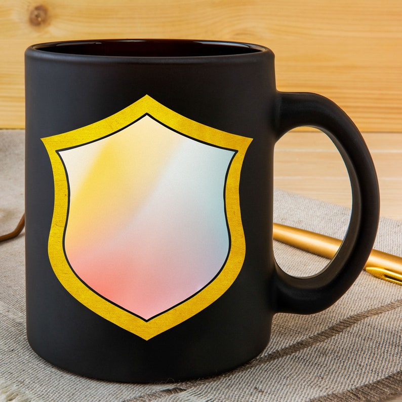 Puede incluir: Taza de cer&aacute;mica negra con un dise&ntilde;o de escudo dorado. El escudo tiene un degradado de rosa, naranja y amarillo.