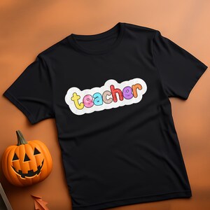 May include: Black t-shirt with a white cloud graphic that says "teacher" in colourful letters.