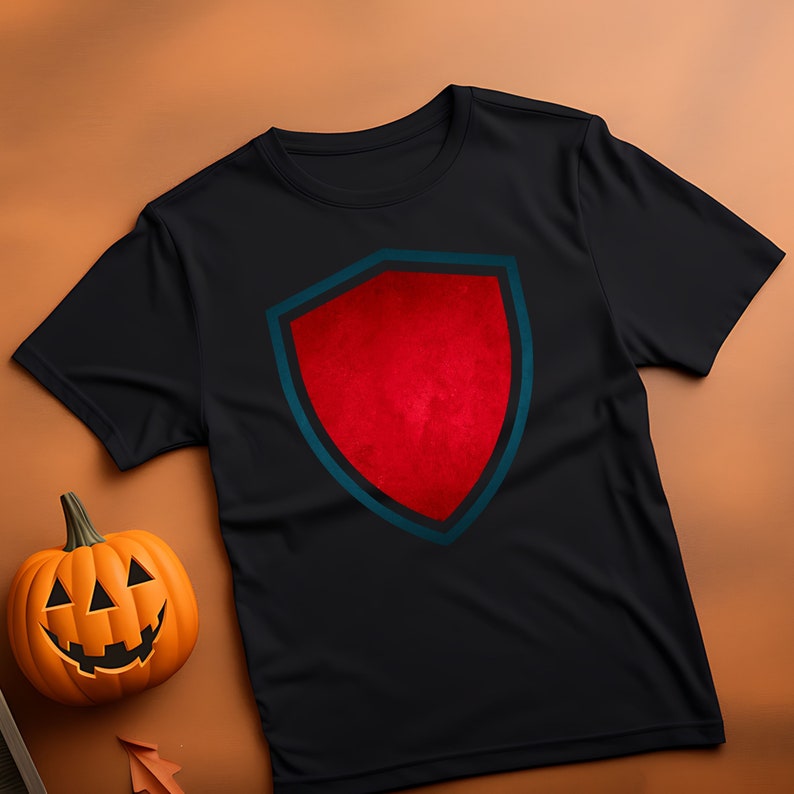 Puede incluir: Camiseta negra con un dise&ntilde;o de escudo rojo. El escudo tiene un contorno azul oscuro y un contorno interior azul claro.