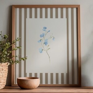 May include: A framed watercolor print featuring delicate blue flowers on a white background. The frame is light brown, set against a striped backdrop. A wooden bowl and a vase with greenery are on a wooden surface.