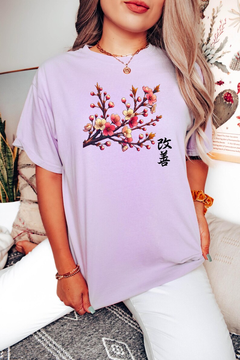 Op de afbeelding: Een lavendelkleurig T-shirt met een bloemenprint en het Japanse woord "桜" (Sakura) dat op de voorkant is gedrukt.