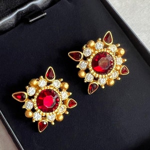 May include: A pair of gold earrings with red and white gemstones. The earrings are in a black velvet box.
