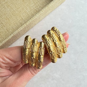 Puede incluir: Un par de pendientes de clip de tono dorado con un diseño texturizado y geométrico.