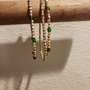 May include: Three gold beaded bracelets with green glass beads. The bracelets are stacked on a wooden dowel.
