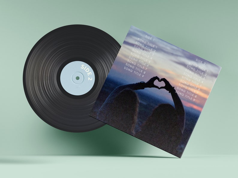 May include: A black vinyl record with a blue label that says "SIDE 2". The record is next to a square album cover with a photo of a person making a heart shape with their hands in front of a sunset. The album cover has a list of song titles on both sides.