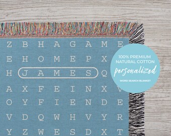 May include: A blue word search blanket with the name "JAMES" highlighted. The blanket is made of 100% premium natural cotton and is personalized. The text "100% Premium Natural Cotton Personalized Word Search Blanket" is printed on a light blue circle.