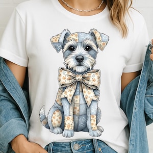 Peut inclure: T-shirt blanc avec une illustration d'un chien Schnauzer assis. Le chien est bleu clair avec des détails de patchwork et des motifs floraux. Il porte un grand nœud beige à motifs floraux.