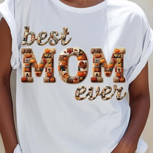 Könnte beinhalten: Weißes T-Shirt mit dem Schriftzug "best MOM ever" in einem Patchwork-Design. Die Buchstaben sind mit herbstlichen Mustern gefüllt, darunter Kürbisse, Blätter und eine Truthahn. Ein lässiges Kleidungsstück für den Alltag.