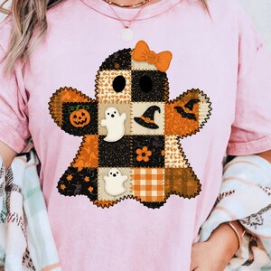 Könnte beinhalten: Rosafarbenes T-Shirt mit einem Patchwork-Geist-Design mit Halloween-Motiven. Der Geist hat eine Schleife, einen Kürbis, einen Hexenhut und andere festliche Details. Das Design verwendet Orange, Schwarz und Weiß.