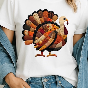May include: White t-shirt with a turkey design. The turkey is made up of a patchwork of autumnal colours, including brown, orange, and red, with a black outline. The design is centered on the shirt, making it a festive apparel choice.