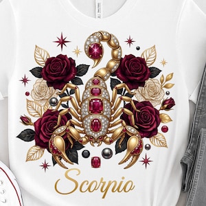 May include: White t-shirt featuring a gold and jewel-encrusted scorpion design, surrounded by burgundy roses and gold floral accents. The word "Scorpio" is written in gold script below the scorpion.
