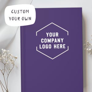 May include: A purple notebook with the text "CUSTOM YOUR OWN" in a white bubble and "YOUR COMPANY LOGO HERE" in a white hexagon. The notebook is on a white surface with white flowers.