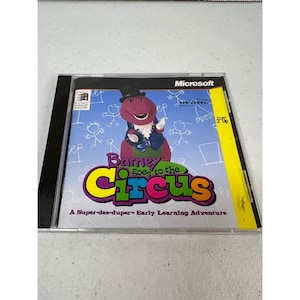May include: A Microsoft CD-ROM case for the game Barney Goes to the Circus, A Super-dee-duper Early Learning Adventure. The cover features a purple dinosaur wearing a black top hat against a light blue background with white line drawings.