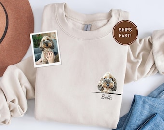 May include: Cream-colored sweatshirt featuring a dog portrait and the name "Bella" below. A small photo of the dog is also on the sweatshirt. The text "SHIPS FAST!" is in a brown circle.