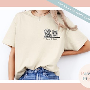 May include: A beige t-shirt with a black and white illustration of a dog and cat. The text "Luna & Daisy" is printed below the illustration.