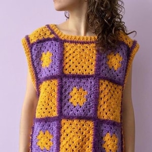 May include: A sleeveless crochet vest featuring a checkerboard pattern of alternating bright yellow and purple squares. Each square is crafted with a textured granny square stitch, and the garment has a wide, rounded neckline and arm openings.