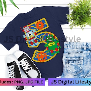 May include: A navy blue t-shirt featuring a robot-themed "5" design, paired with black and white trainers and denim shorts. The design includes a red and blue robot, a green robot, and orange cogs. Text on the shirt reads "JS Digital Lifestyle".