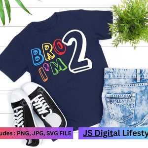 May include: A navy blue t-shirt with the text "BRO I'M 2" in colourful letters. The number 2 is white and outlined in black.