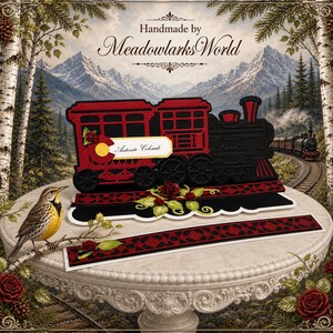 May include: A red and black papercraft train with the text "Antonite Colorado". The image features a mountain backdrop and a bird on a branch. The train is a decorative item.