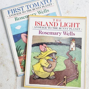 Puede incluir: Se muestran dos libros infantiles de Rosemary Wells. El libro superior se titula "First Tomato" y el inferior "The Island Light". Ambos libros presentan ilustraciones coloridas, incluyendo un personaje de conejo y un faro.