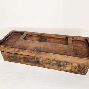 May include: A rustic wooden organizer with three recessed compartments. The wood has a warm, brown tone with visible grain and a distressed finish. The word "WILSON" is carved into the wood. Ideal for desk organization or as a decorative piece.
