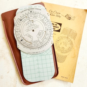 May include: A vintage Kane Aero Co. MK-6B Dead Reckoning Computer in a brown leather case. The computer has a circular slide rule with a gridded chart on the back. The case includes a small instruction booklet titled "On Course Kane Way".
