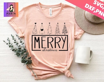 May include: A light pink t-shirt with a black graphic that says "MERRY christmas" inside a black rectangle. Above the text are five stylized Christmas trees. A white mug and a hat are in the background.