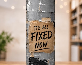 May include: A cylindrical tumbler with a straw featuring a graphic print of overlapping silver and black duct tape strips. A central tan rectangular patch with torn edges displays the black text ITS ALL FIXED NOW in a bold, hand-lettered style.
