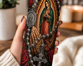 May include: A cylindrical tumbler with a metal straw featuring a religious graphic print of the Virgin of Guadalupe, praying hands, a silver rosary with a crucifix, and deep red roses against a dark, ornate background with golden light rays.