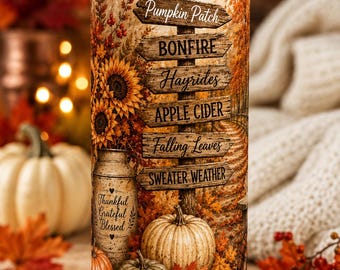 May include: A cylindrical tumbler with a clear lid and metal straw featuring an autumn-themed print. The design includes a wooden signpost with text reading Pumpkin Patch, BONFIRE, Hayrides, APPLE CIDER, Falling Leaves, and SWEATER WEATHER.