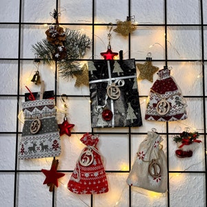 May include: A black grid wall display featuring a Christmas advent calendar with fabric pouches and a wrapped gift. The items are decorated with wooden number tags, red and white patterns, pine branches, gold stars, and warm string lights.