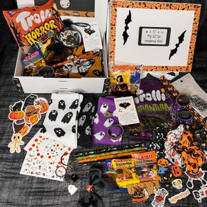 Può includere: Una confezione regalo a tema Halloween traboccante di dolcetti e accessori. Include calzini con fantasmi, adesivi, caramelle e una varietà di altri oggetti spettrali. La scatola è decorata con pipistrelli e le parole "My little Seasons Box".