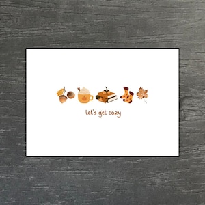 Könnte beinhalten: Eine weiße Karte mit Herbstillustrationen: Eicheln, ein Kürbis-Latte, Bücher, Socken und ein Blatt. Der Satz "let's get cozy" steht in brauner Schrift unter den Illustrationen.