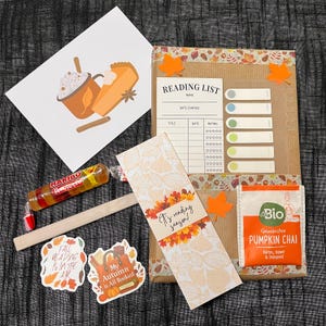 May include: A reading-themed gift set featuring a brown paper-wrapped book, a reading list card, a bookmark with autumn leaves and the text 'It's reading season!', two stickers, a Haribo Roulette candy roll, and a packet of Pumpkin Chai tea.