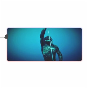 Può includere: Un subacqueo con una muta da subacquea nera e attrezzatura da sub è sott'acqua, tenendo un fucile da pesca subacquea. L'acqua è di un blu vibrante.