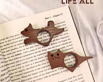 May include: Two wooden book page holders in the shape of a squirrel and a cat rest on an open book. The squirrel and cat are brown with a hole for a finger. The book is open to Chapter 22.